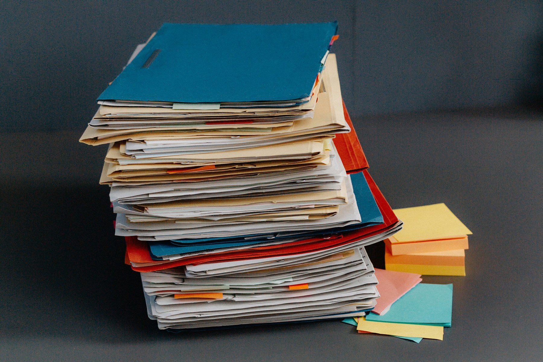 Pile de dossiers et chemises mélangés avec post-it et fiches volantes — image de la dispersion documentaire avant méthode.