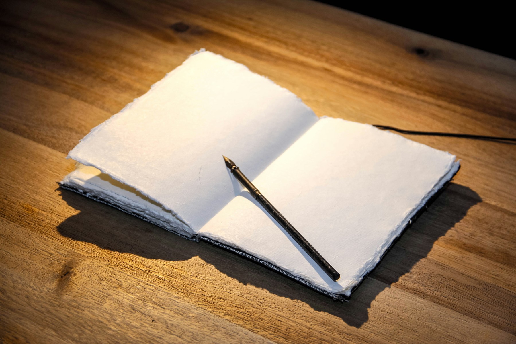 Carnet ouvert aux pages déchirées à la main, stylo-plume noir à plume dorée posé en diagonale, bureau en bois, lumière latérale chaude.