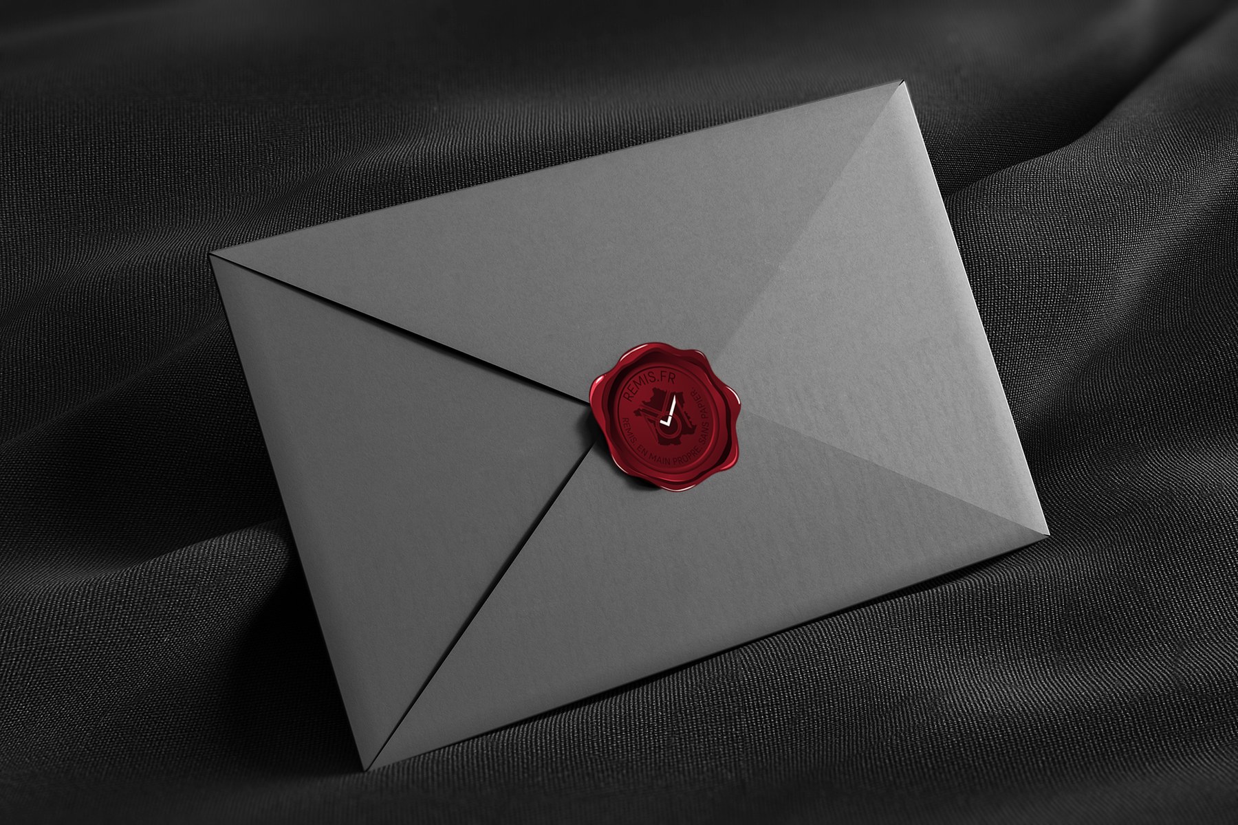 Enveloppe gris anthracite scellée par un cachet de cire rouge marqué Remis, posée sur soie noire.